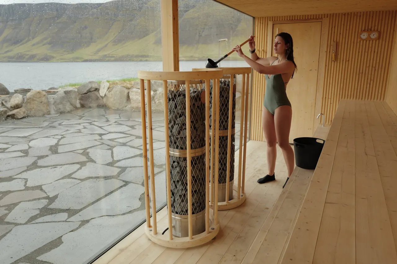 Woman pouring water on the sauna stones, with a view of the fjord